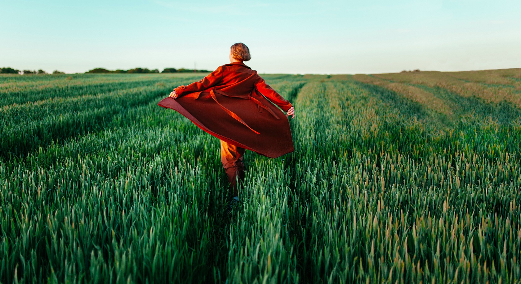 Woman in red coat walking in the field at sunset